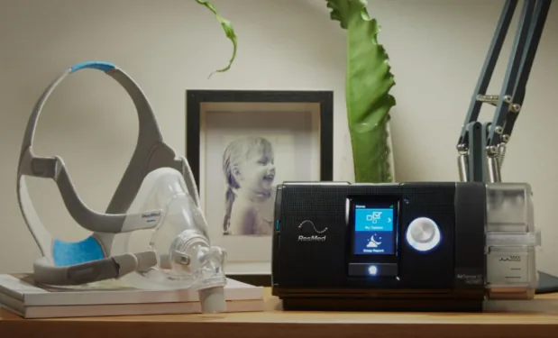 Appareil CPAP ResMed sur une table de nuit, à côté d'un masque AirFit